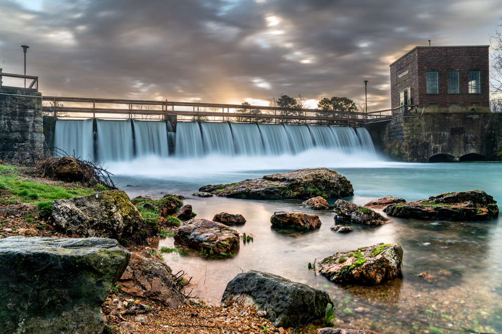 A dam a state park in Arkansas that creates a beautiful waterfall at dusk with an old structure. 