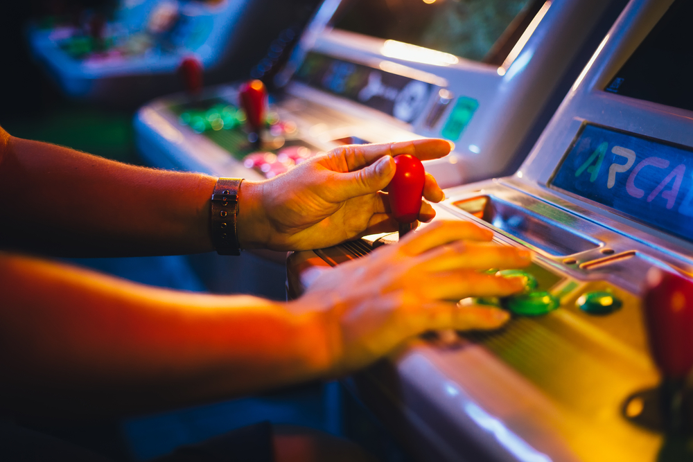 One of the most fun things to do in Greensboro at night is go to Boxcar Bar and Arcade. Pictured is a person playing a classic arcade game, holding the controls.