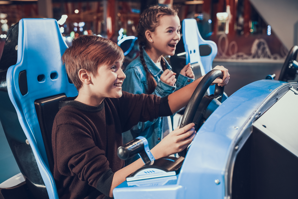 Brother and sister playing a race car video game in an arcade at one of the fun amusement parks in Georgia. 