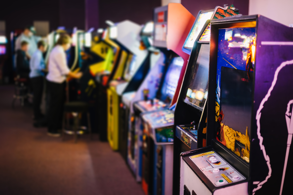 A line of arcade cabinets with some guest playing the game in the background in a full arcade at one of the theme parks in Georgia. 