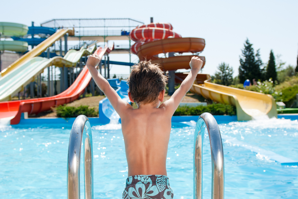 Boy cheering on riders of dueling water slides at one of the amusement parks in Georgia. 