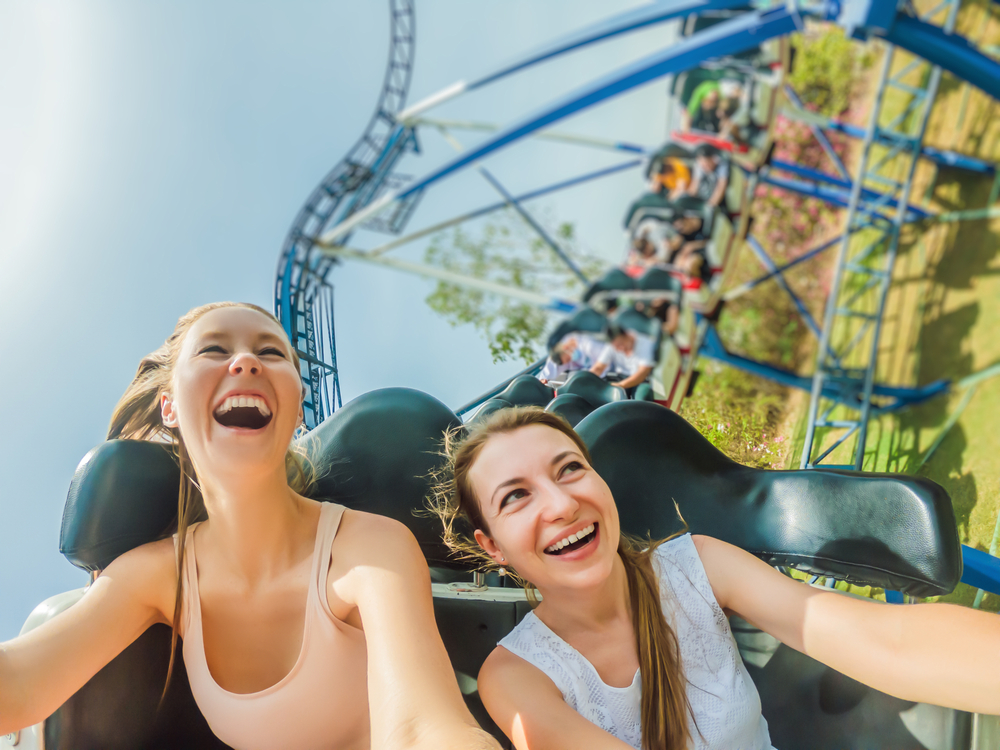 Two girls laughing and smiling on an outdoor steel roller coaster at one of the amusement parks in Georgia. 