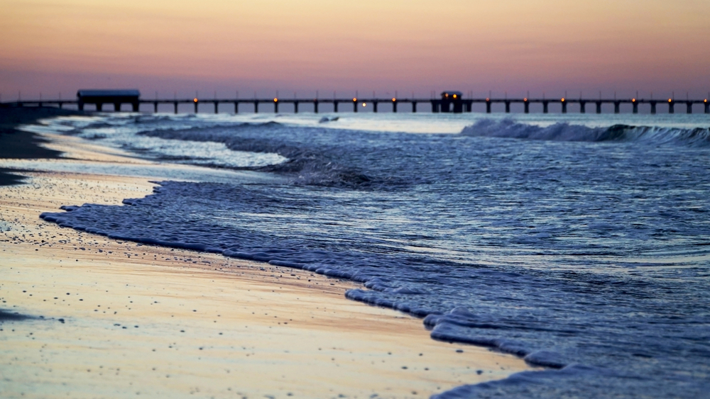 crashing waves on beach with pier in background