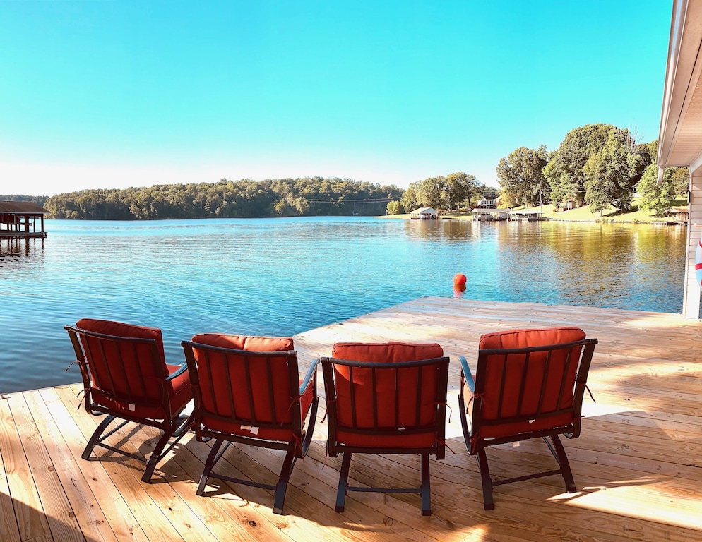 View of 4 cushy orange chairs on a dock facing out to a beautiful blue lake. 