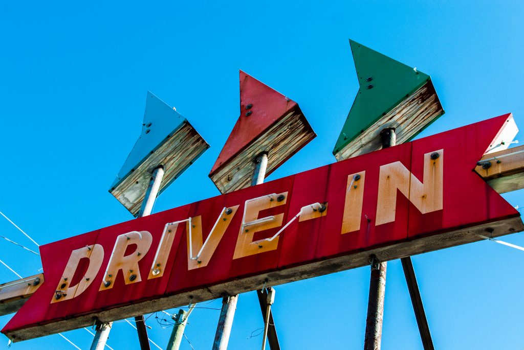 A classic Drive-in movie theater sign that is red with neon letters and blue, red, and green arrows on top of it. 