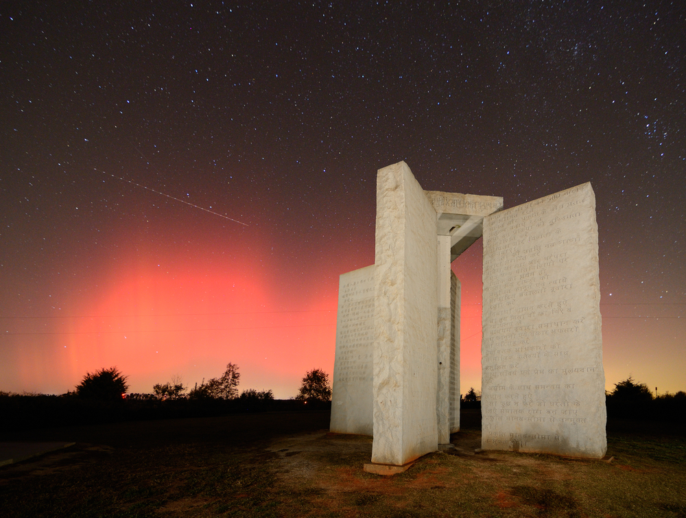 Four tall granite slabs standing next to each other. You can see stars in the sky and it is a little pink from the sunsetting. It is a long exposure photo. 