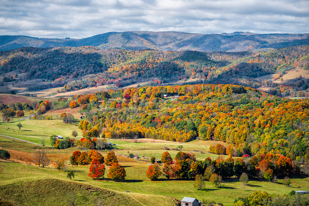 A view of the rolling hills in Virginia's Highland County. There are trees with green, red, yellow, and orange leaves and large meadows. 