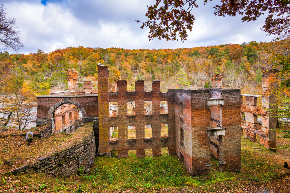 The brick ruins of burned down mill from the 1800's. It is surrounded by woods where the trees are changing colors. 