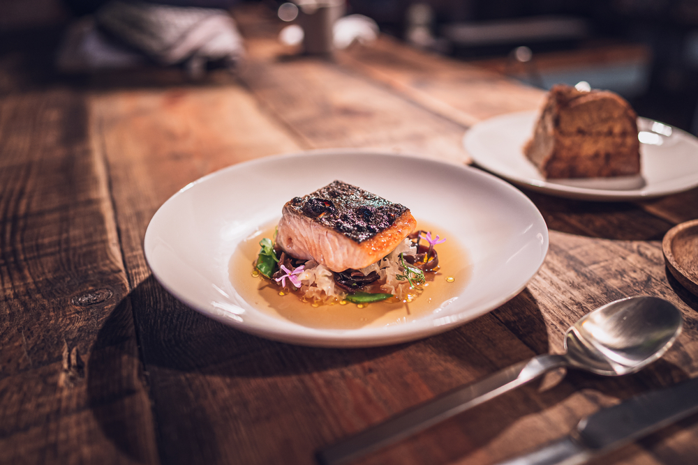 A fish dish over roasted veggies served in a bowl with broth