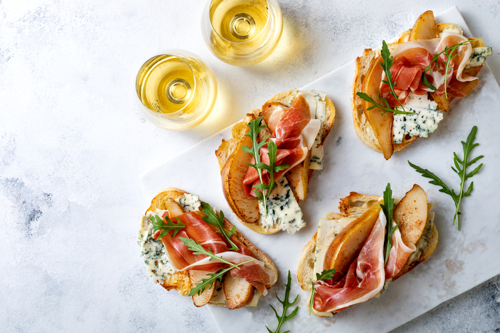 Sample prosciutto toast with blue cheese and roasted pear on a marble table with white wine
