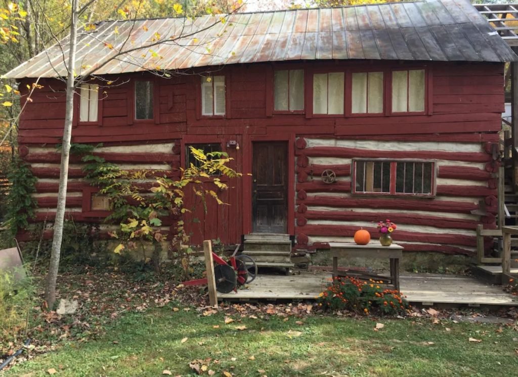 The exterior of a really old log cabin style barn that is painted red with white mortar between the wood beams. 