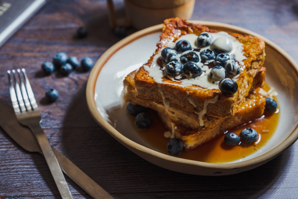 A warm stack of french toast drizzled in maple syrup. Topped with fresh cream and blueberries. The best french toast in Atlanta.