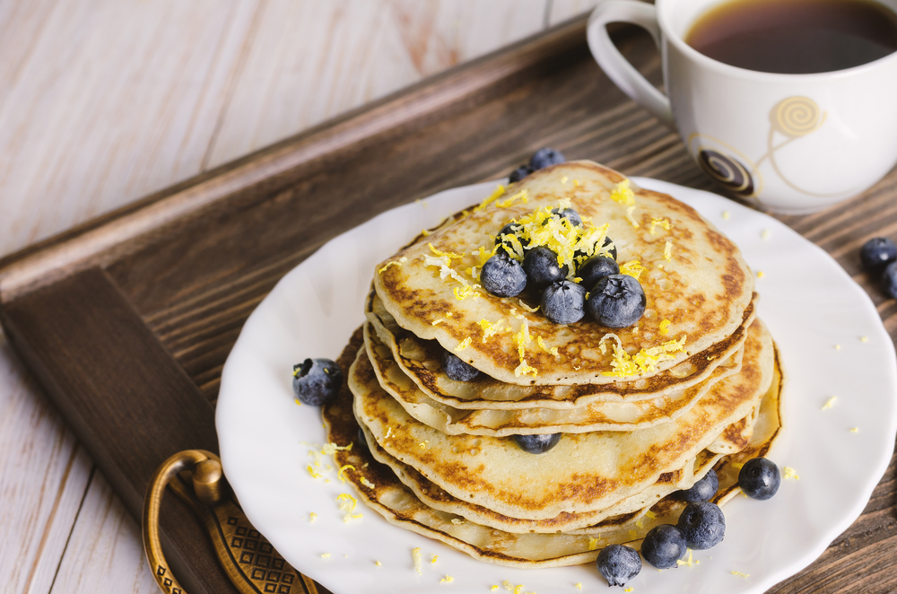 A stack of pancakes sits on a plate, topped with lemon zest and blueberries, like the order served at Another Broken Egg Cafe in Charleston.