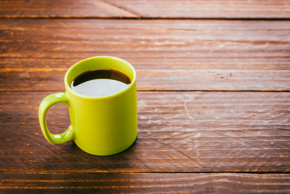 A bright yellow-green mug full of coffee on a wooden surface, like at the Junction in Charleston, SC.