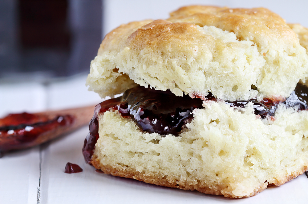 A buttermilk biscuit with berry jam on a white background, like those served at Callie's Hot Little Biscuit in Charleston.