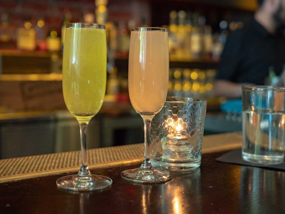 One orange and one grapefruit mimosa sit on a wooden bar, like those served at Daps for breakfast in Charleston.