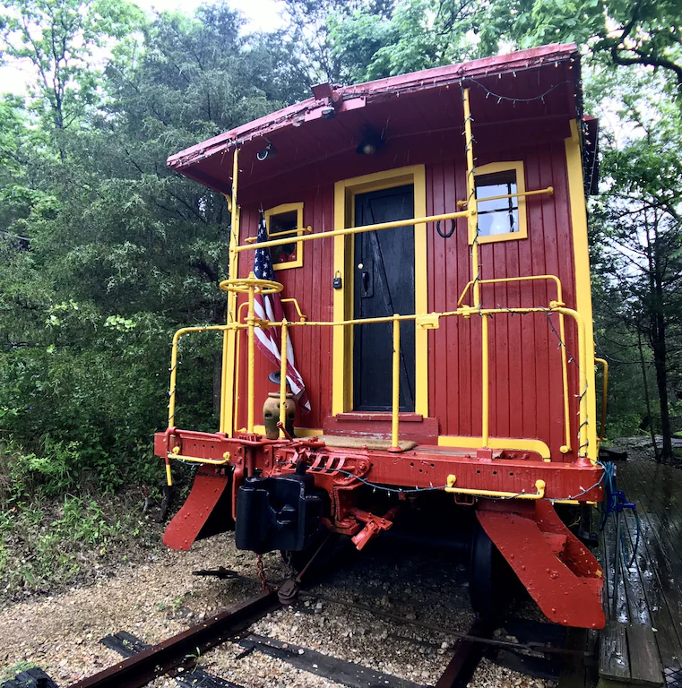 A red and yellow train carriage set in thick woods and decorated with a USA flag. 