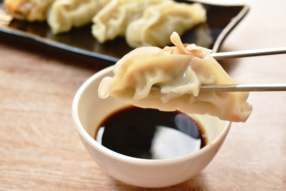 Close up photo of a steamed dumpling being held by chopsticks over a bowl of soy sauce. The dumplings at Dumplings and Beyond make them one of our favorite restaurants in Georgetown DC!