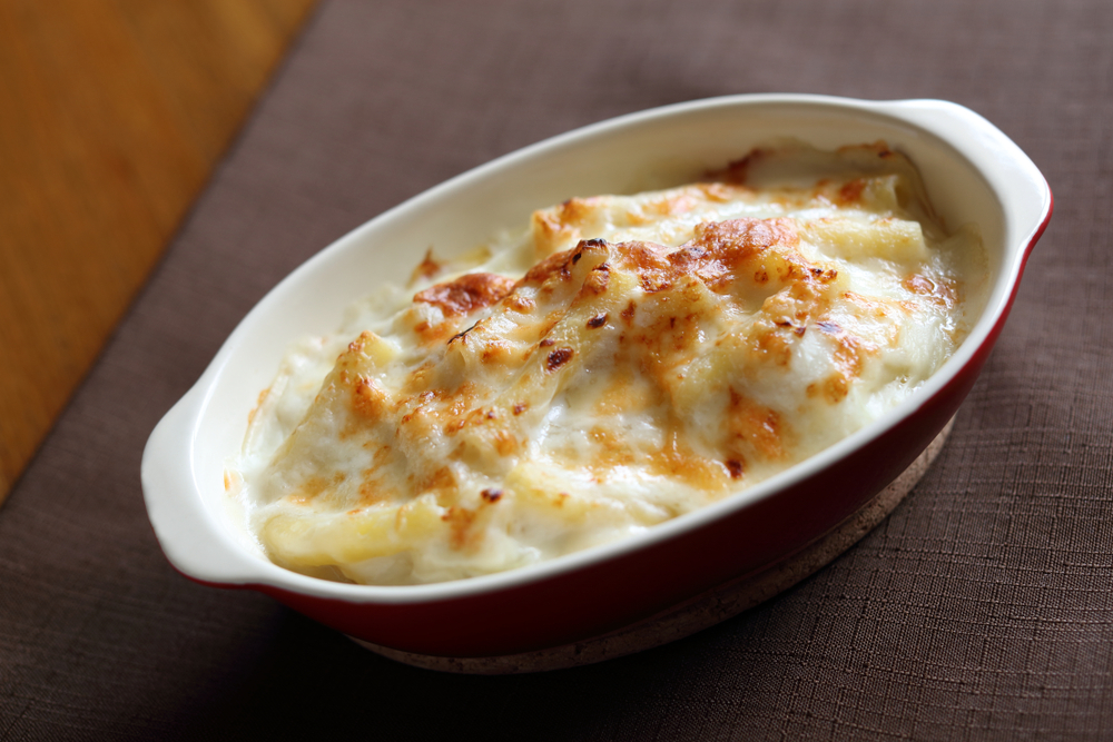 A dish of macaroni au gratin in a red bowl on a brown placemat. This dish is one of our favorites at Chez Billy Sud, one of the best restaurants in Georgetown DC. 