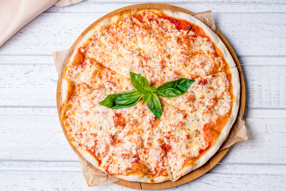 A margherita pizza sits on a board on a white table. 