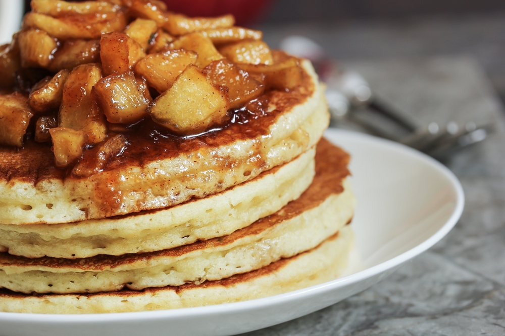 A stack of apple pancakes sits on a white plate.