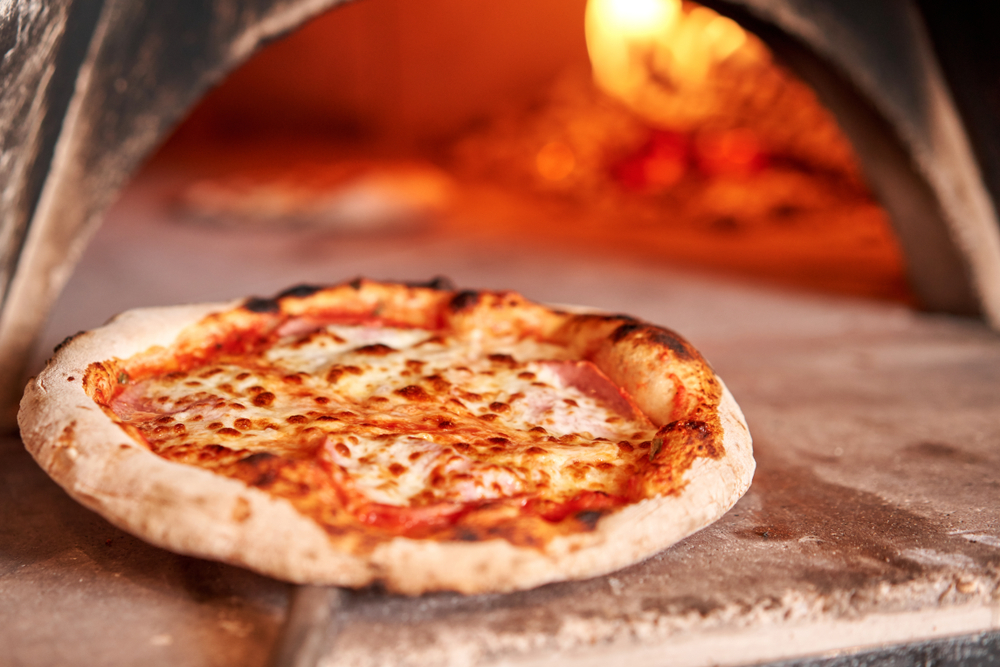 A bubbly cheese pizza is being taken out of a woodfire oven.