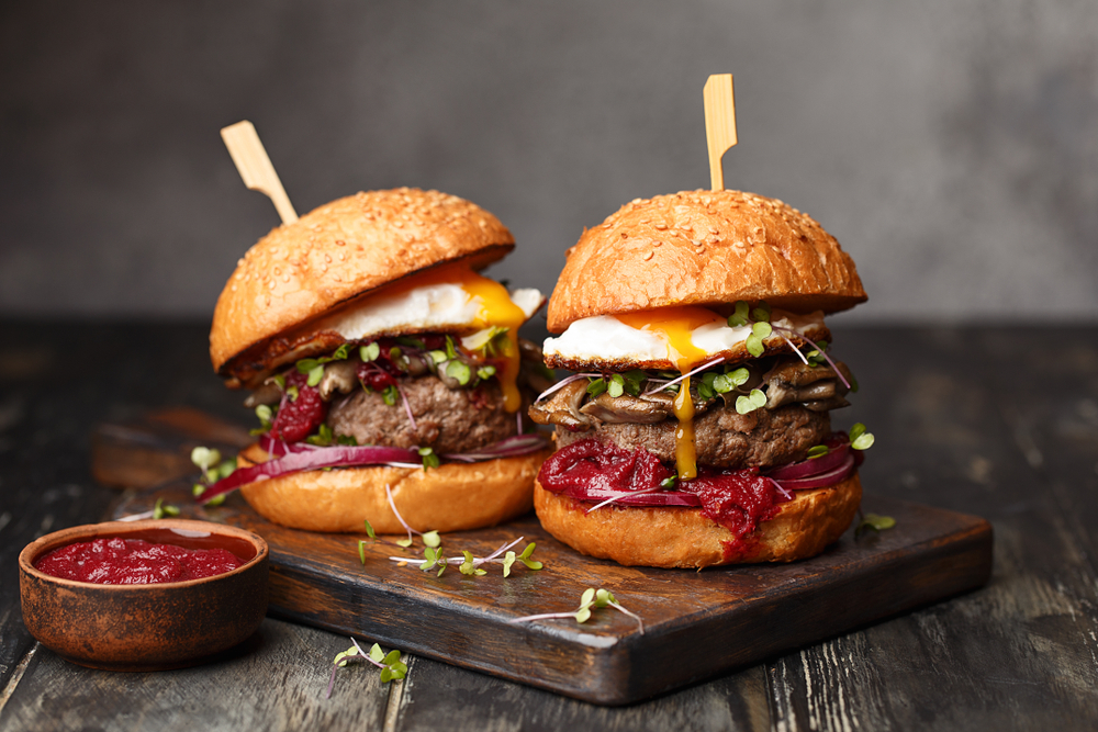 photo of two burgers with runny fried eggs on a wood cutting board 