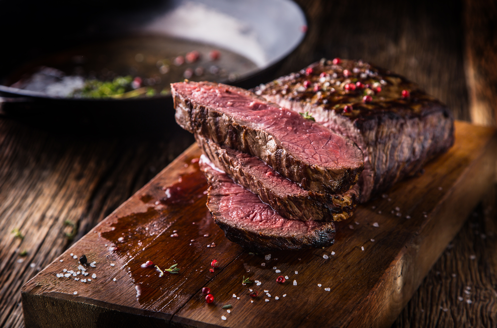 Steak is cut on a wooden board, cooked pink on the inside, but crispy on the outside, showing the perfection that some of the  best restaurants in San Antonio have!