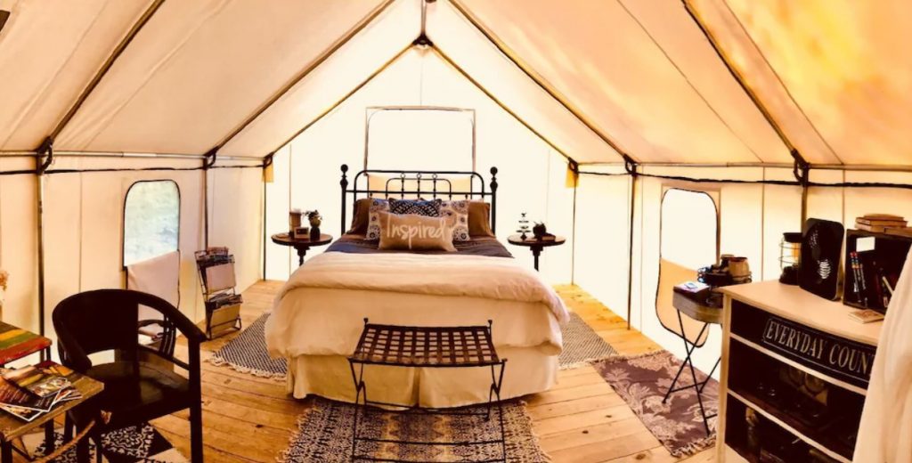 The interior of a canvas tent that has a queen-sized bed, seating, rugs, and a coffee station. A unique spot for glamping in North Carolina