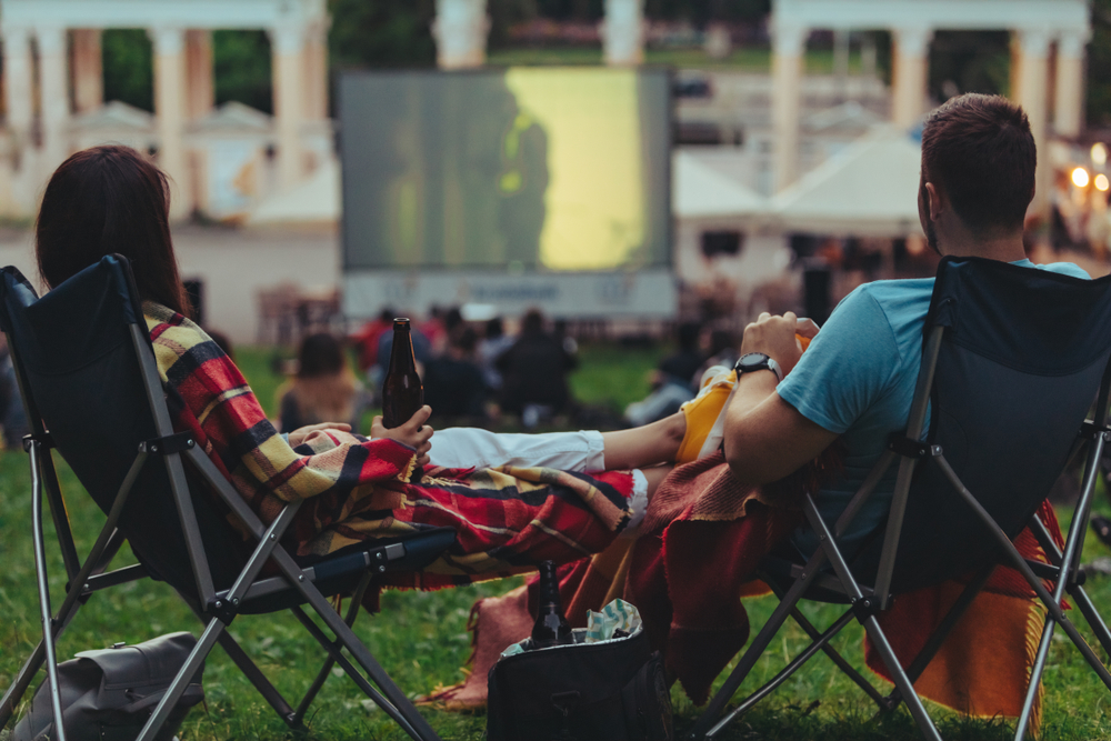 couple sitting in lawn chairs watching an outdoor movie on a big screen 