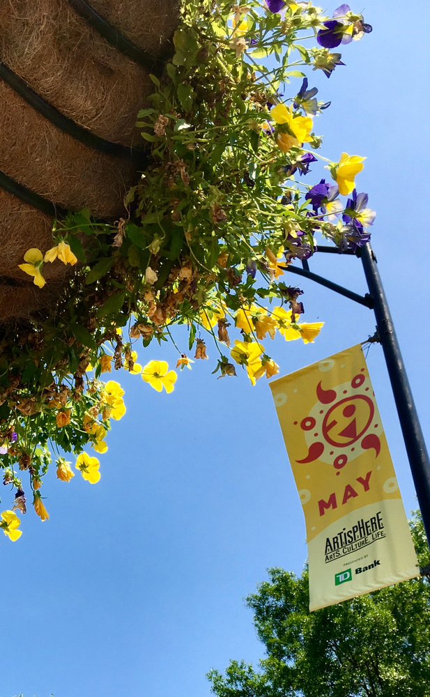 Yellow flowers in a hanging basket next to a street lamp banner advertising Artisphere, one of the best annual events and things to go in Greenville SC
