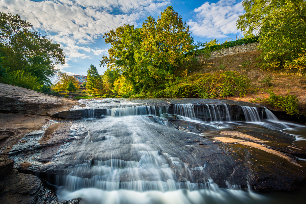 A short waterfall across wide granite rocks with bright green trees on the surrounding banks