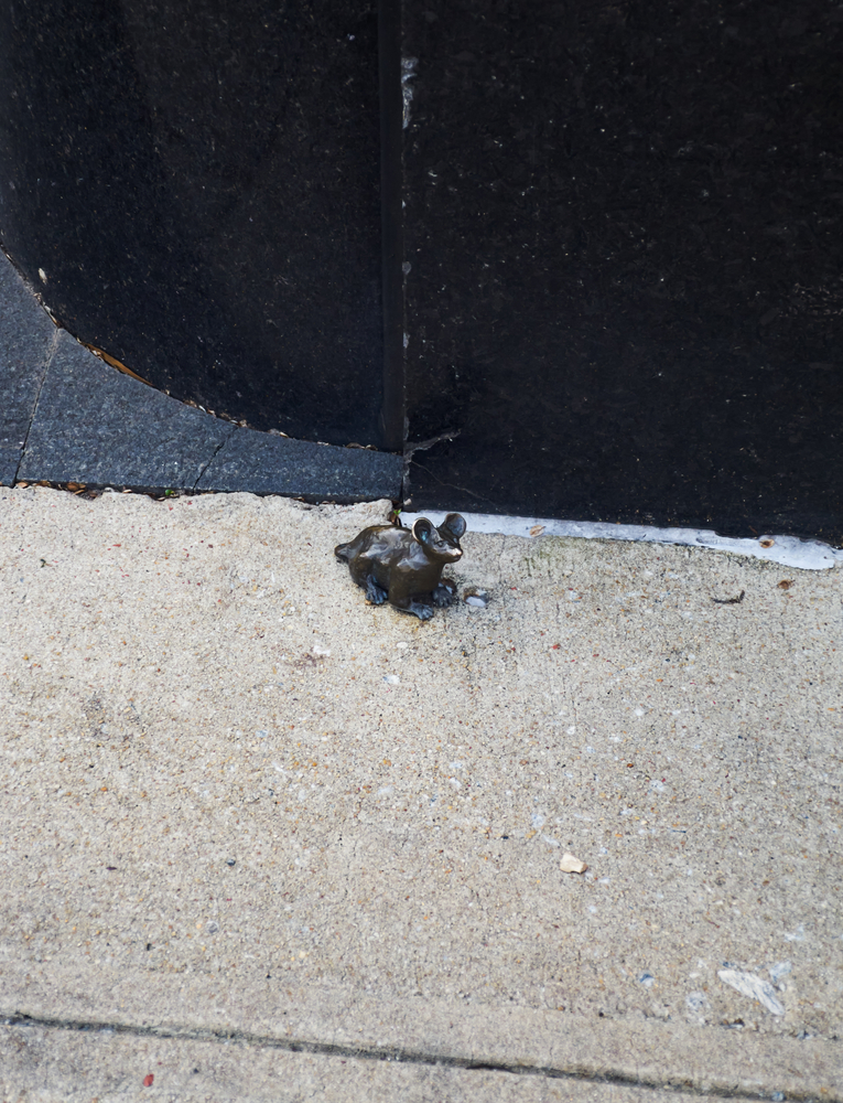 A tiny bronze mouse sits on the concrete pavement as part of the Mice on Main Scavenger Hunt in Greenville SC