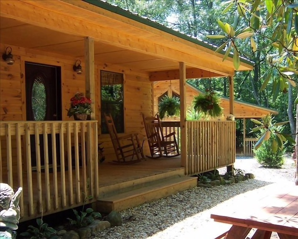 A wooden cedar cabin wth a flat roof and a porch. There are tropical green leaves in the background of the best North Georgia cabins you must visit.