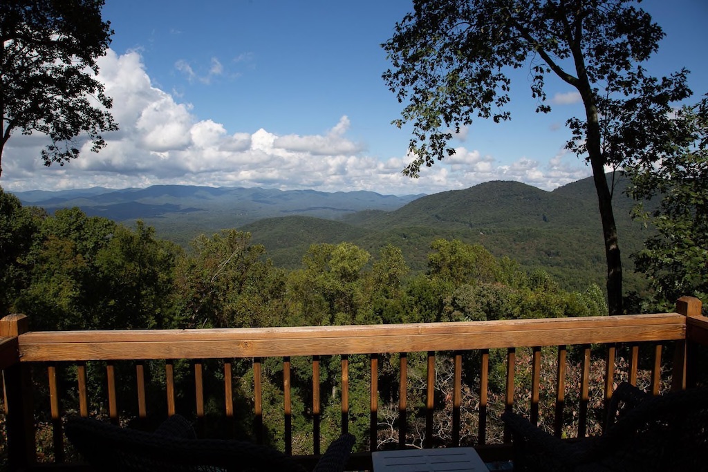 A wooden rail at one of the best northern Georgia cabin rentals. Overlooking lush green mountains and a blue sky.