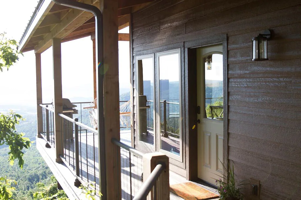 A wooden cabin set high up overlooking a valley. There is a hammock and barbeque for glamping in Arkansas