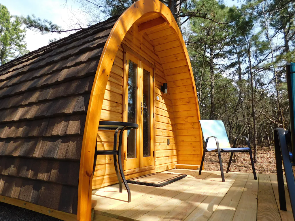 A circular cabin with roof tiles encircling it, the front deck features outdoor furniture one of the places for glamping in Arkansas