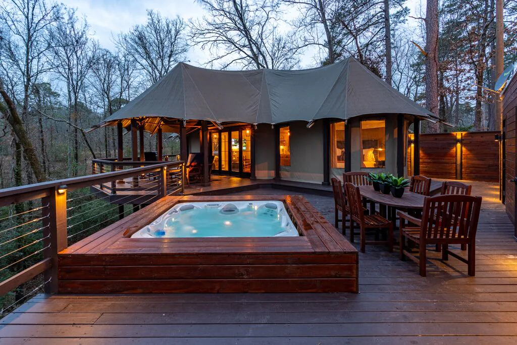 A hot tub and outdoor dining set on wooden decking in front of a luxury tent surrounded by trees one of the best places for glamping in Arkansas