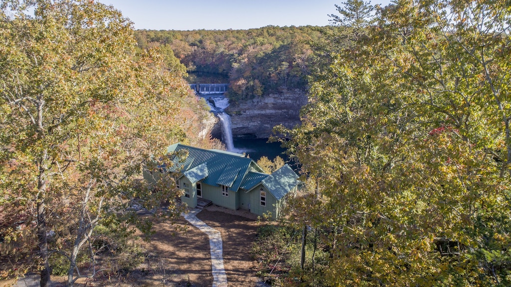 View of the small green cabin and striking waterfall behind it. 