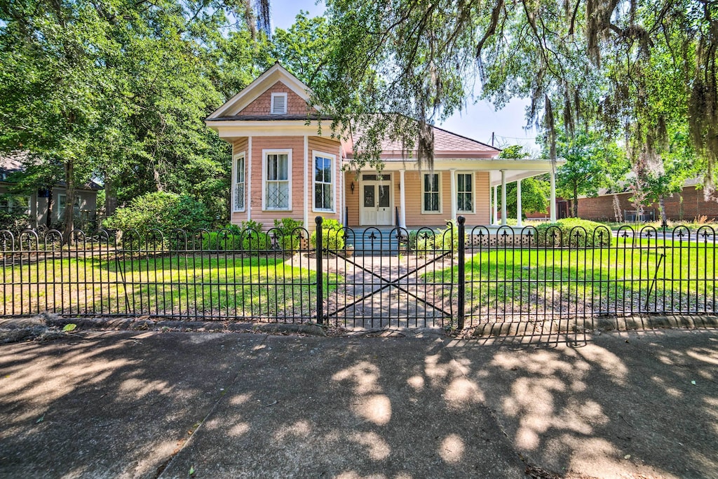 view of the front yard, wraparound porch and bay window of this sweet pink home. 