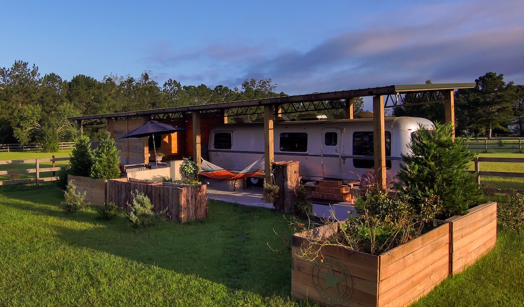 exterior photo showing off the airstream and lovely outdoor area beside a lush green paddock. 