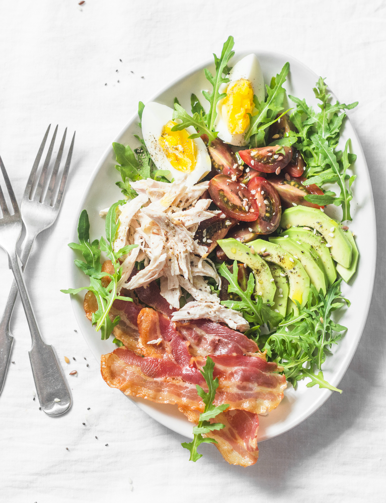 A salad with roasted chicken, avocado, tomatoe, egg and bacon 