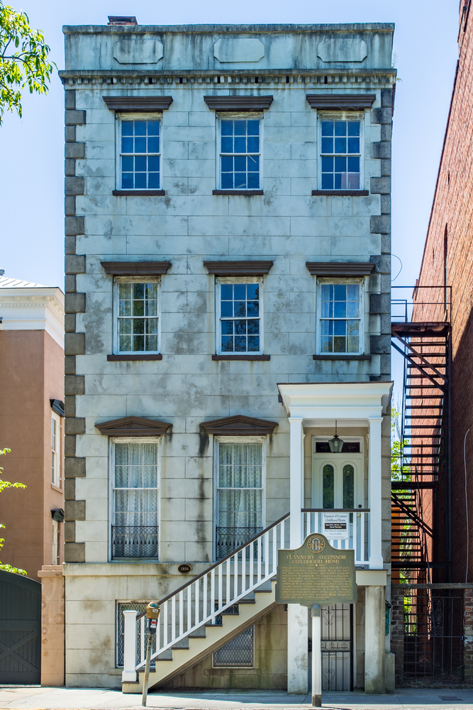 The front exterior of a narrow three story tall building that is the childhood home of Flannery O'Connor. 