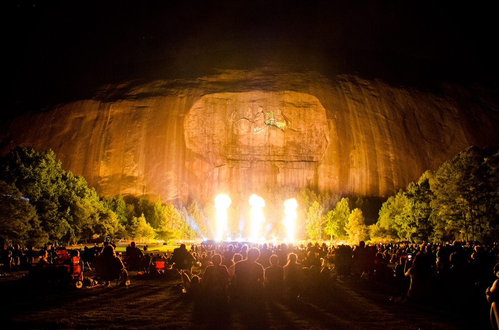 Fireworks dance on the granite of Stone Mountain in front of crowds. The laser show at Stone Mountain is one of the free things to do in Atlanta during the summer! 