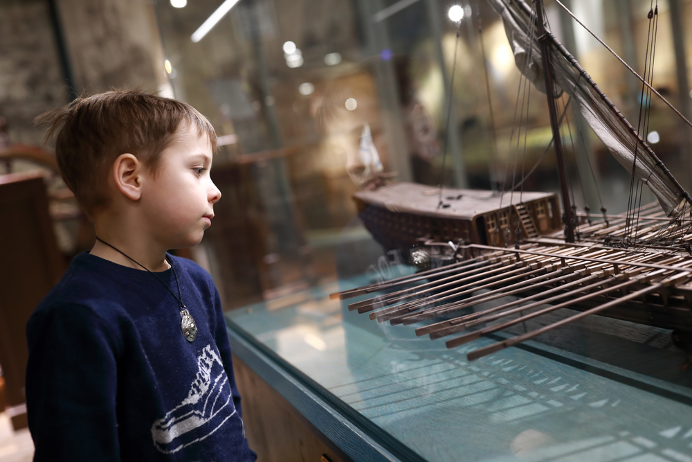 A child looking at a model of a ship in a large glass case. 