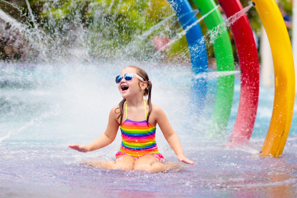 child sitting with sunglasses and bright bathingsuit in a fun water feature at one of the best things to do in Shreveport with kids 