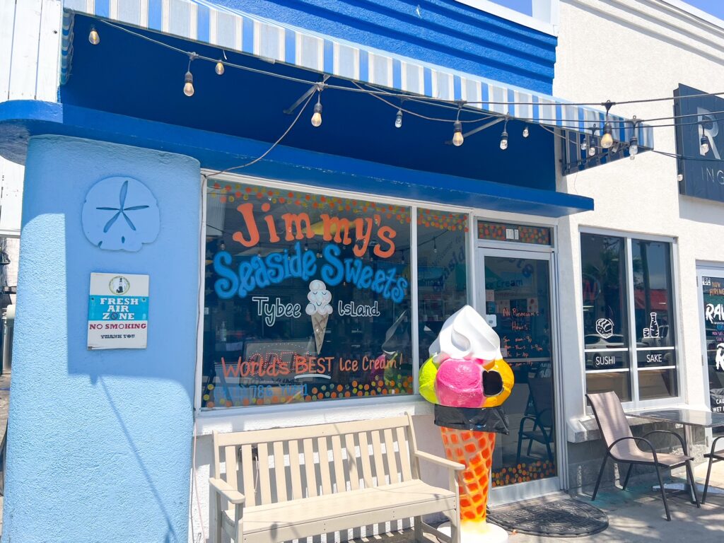 The outside of an ice cream shop. On the window it says Jimmys Seaside Sweets with a large picture of an ice cream. 