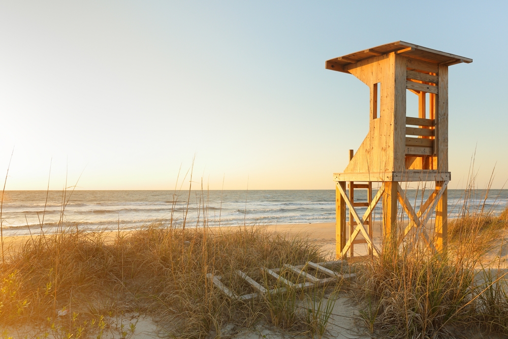A wooden structure with sand and grass on the shores of one of the beach towns in North Carolina.