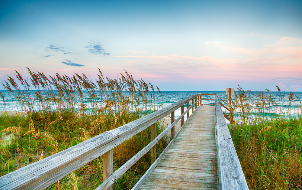 A board walk to the ocean with tall grass. Kure Beach is one of the best things to do in Wilmington NC.