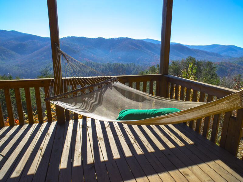 A hammock tied to a wooden balcony amid the mountains in the fall. You can experience the outdoors when you visit North Georgia Cabins